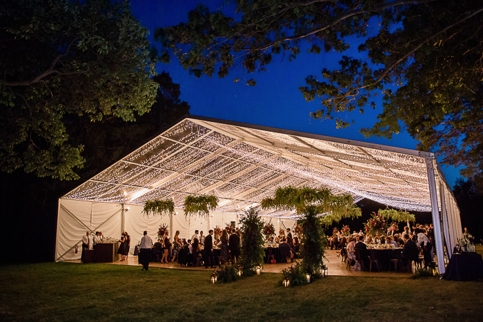 Outdoor tented wedding with greenery chandeliers, blue linens, and lots of string lights
